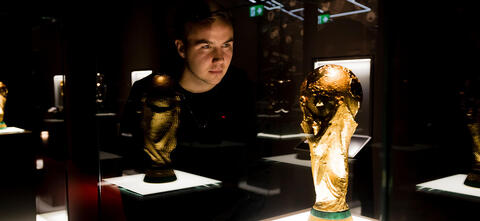 Mario Götze schaut durch die Vitrine in der Schatzkammer des Deutschen Fußballmuseums auf den WM-Pokal 2014