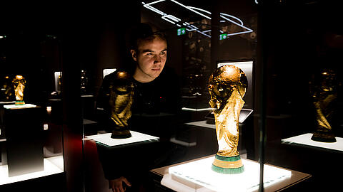 [Translate to en:] Mario Götze schaut durch die Vitrine in der Schatzkammer des Deutschen Fußballmuseums auf den WM-Pokal 2014