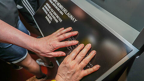 Hände berühren eine Infotafel mit Brailleschrift
