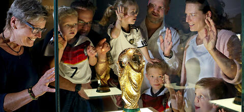 Eine große Familie steht um die Vitrine mit dem WM-Pokal herum