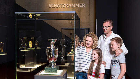 Eine Familie steht neben dem EM-Pokal in der Schatzkammer des Deutschen Fußballmuseums