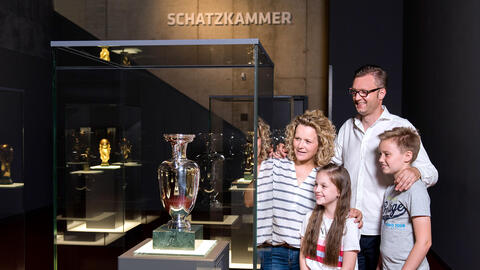 [Translate to en:] Eine Familie steht neben dem EM-Pokal in der Schatzkammer des Deutschen Fußballmuseums