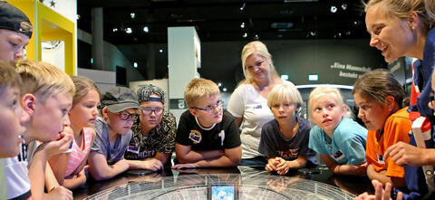 Kinder stehen im Kreis und lauschen gespannt den Worten einer Museumsführerin