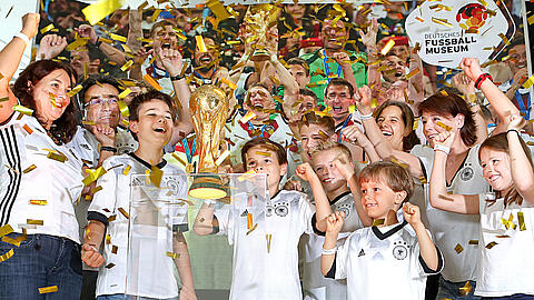Besucher stehen neben dem WM-Pokal und jubeln